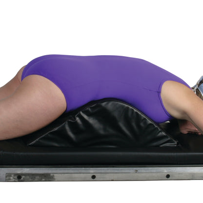 A person lies face down on an AliMed Vinyl-Covered Deluxe Knee Bolster/Lumbar Positioner, wearing a purple suit.