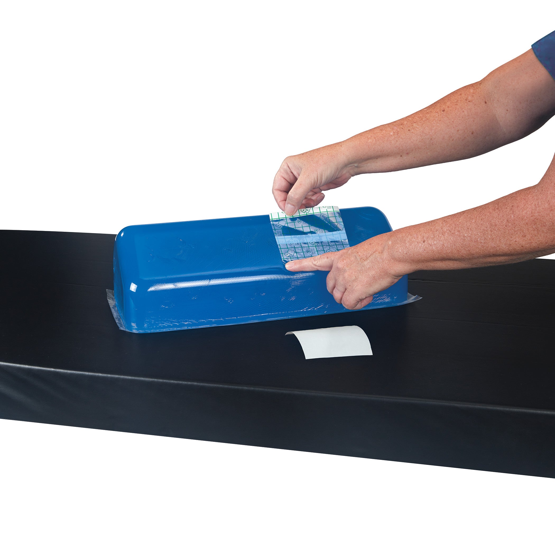 A person uses the AliMed Gel Repair Kit to apply a patch on a blue gel pad on a black surface.