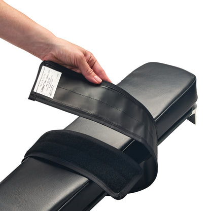 A hand holds the AliMed Reusable Armboard Strap over a black padded armboard, showing the adjustable Velcro strap design.