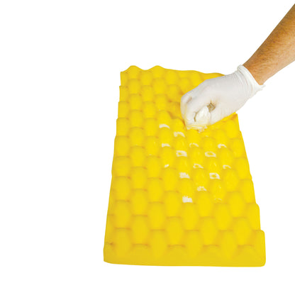 A hand with a glove cleans an AliMed Protecta-Coat Egg Crate Waterproof Ulnar Pad, a yellow, textured pad with white spots.