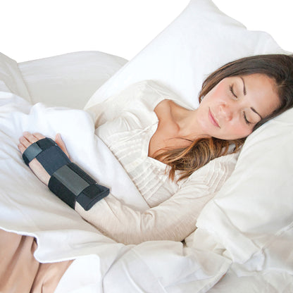 A person sleeps in bed wearing the Brownmed IMAK RSI WrisTimer PM Wrist Support on their right wrist.