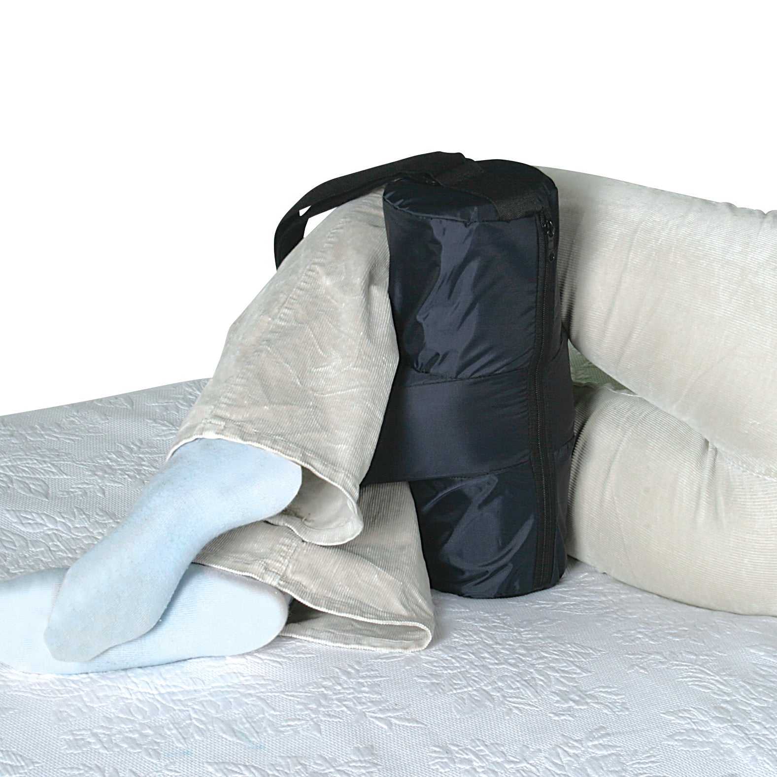 A person with socks uses the SkiL-Care Side-Lying Leg and Knee Abductor between their knees while lying on a patterned surface.