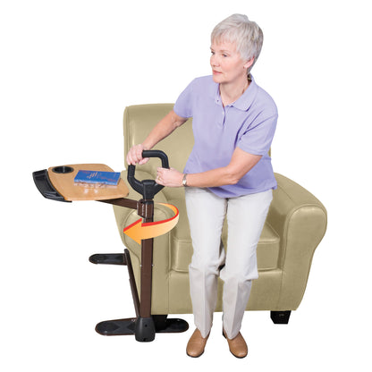 A woman uses an Assist-A-Tray to help stand from a chair, featuring a support handle and a wooden tray with a cup holder.