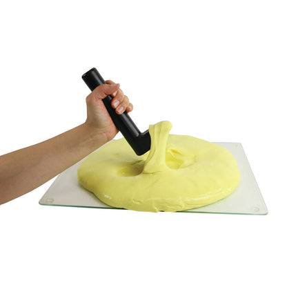 A hand holds a black Puttycise Tool Set handle pressing into yellow putty on a clear surface.