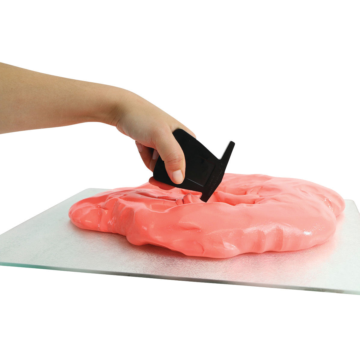 A hand using a Puttycise Tool Set to shape pink putty spread on a flat surface.