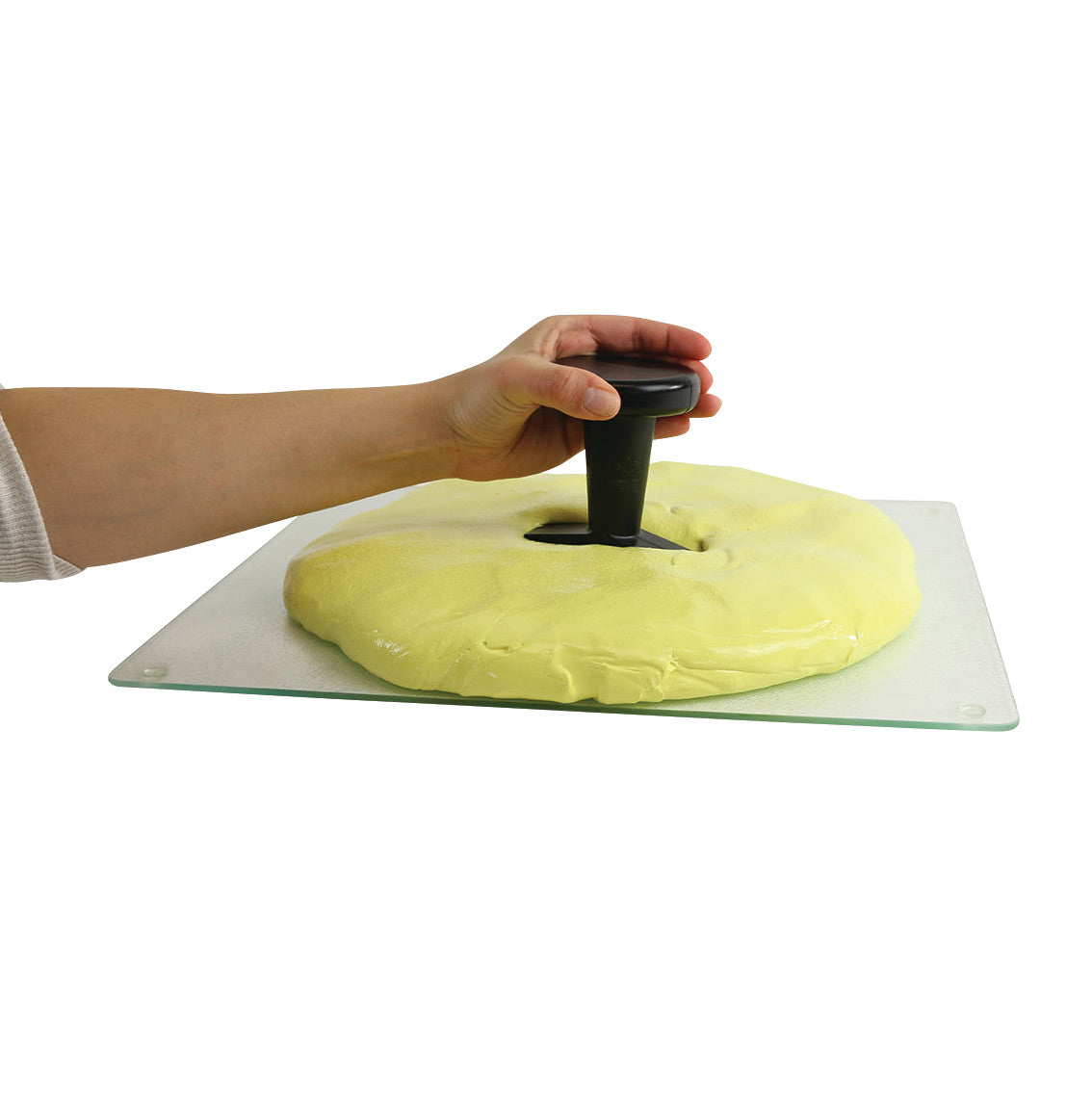 A hand presses a Puttycise Tool Set handle into yellow putty on a flat surface, demonstrating its use for hand therapy exercises.