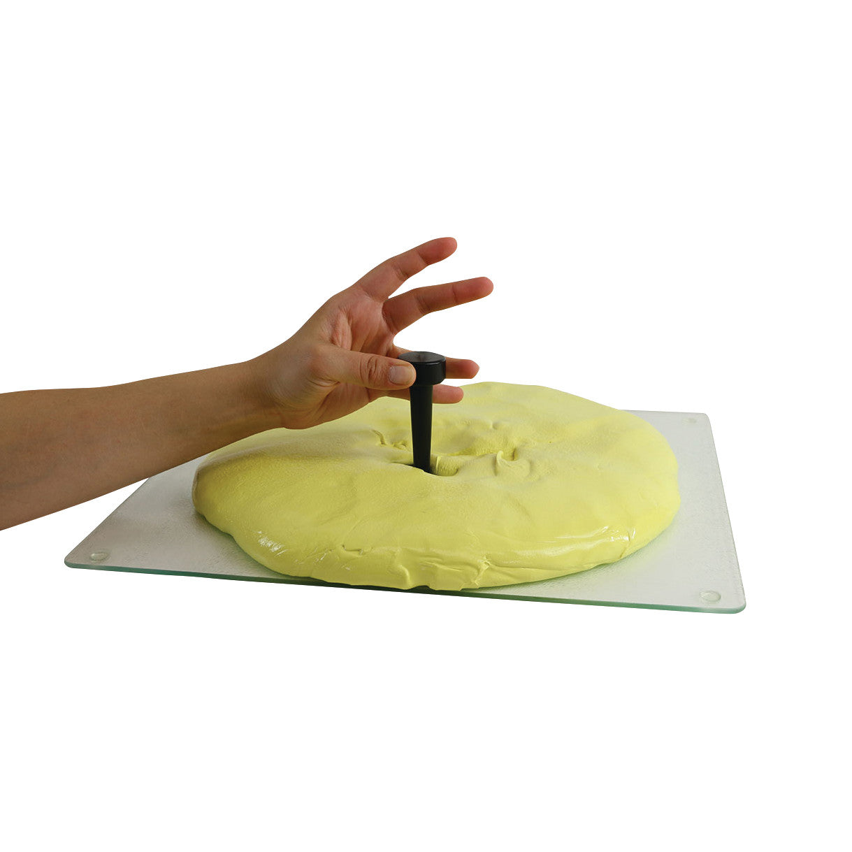 A hand pressing a tool from the Puttycise Tool Set into a flat piece of yellow putty on a glass board.