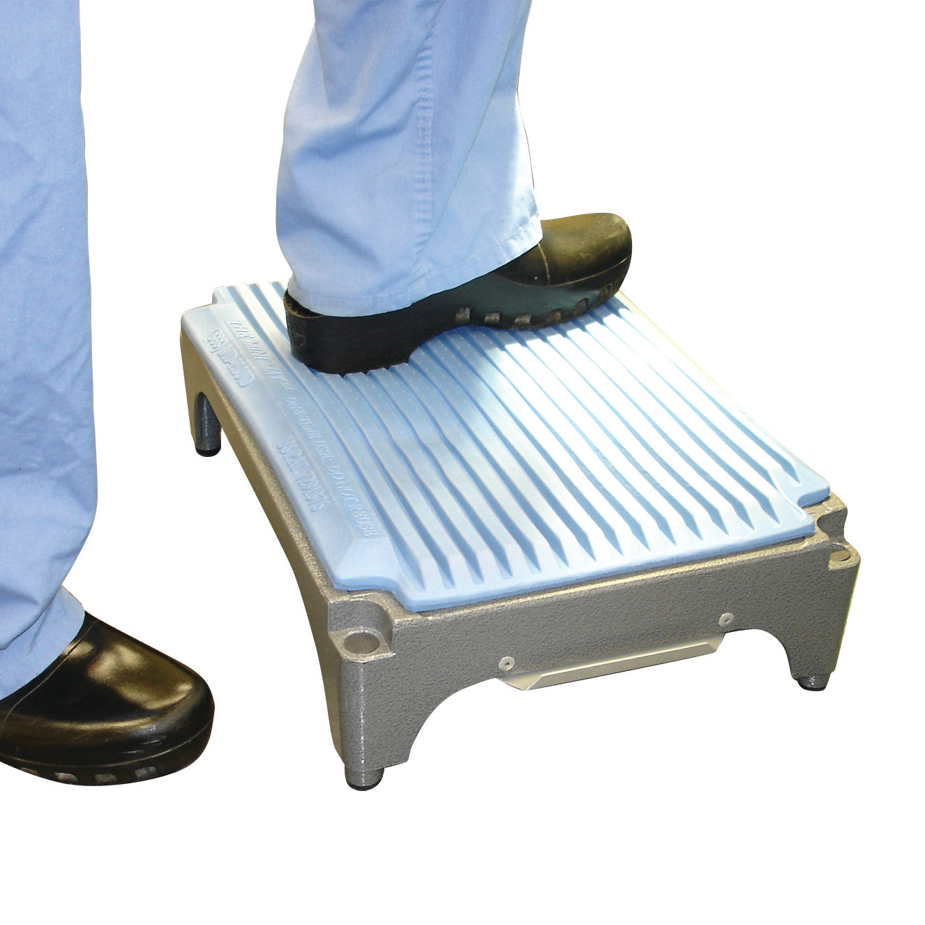 A person steps on a Flagship Surgical Mini Mat wearing blue scrubs and black clogs. The mat has a textured, non-slip surface.