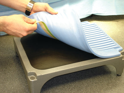 A person is placing the Flagship Surgical Mini Mat on a raised platform, showing its textured, non-slip blue surface.