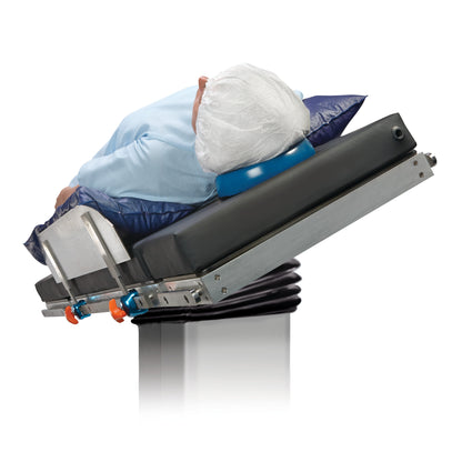 A person in a blue gown is secured on an inclined medical table with an AliMed Lateral Fence, featuring an adjustable head cushion.