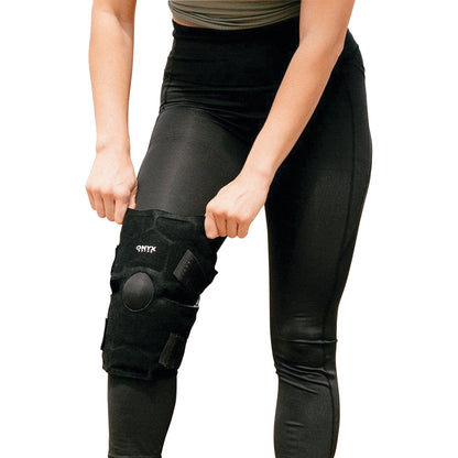 Person adjusting Xena Therapies Onyx Cool Knee brace, wearing black leggings, visible from waist to knee.