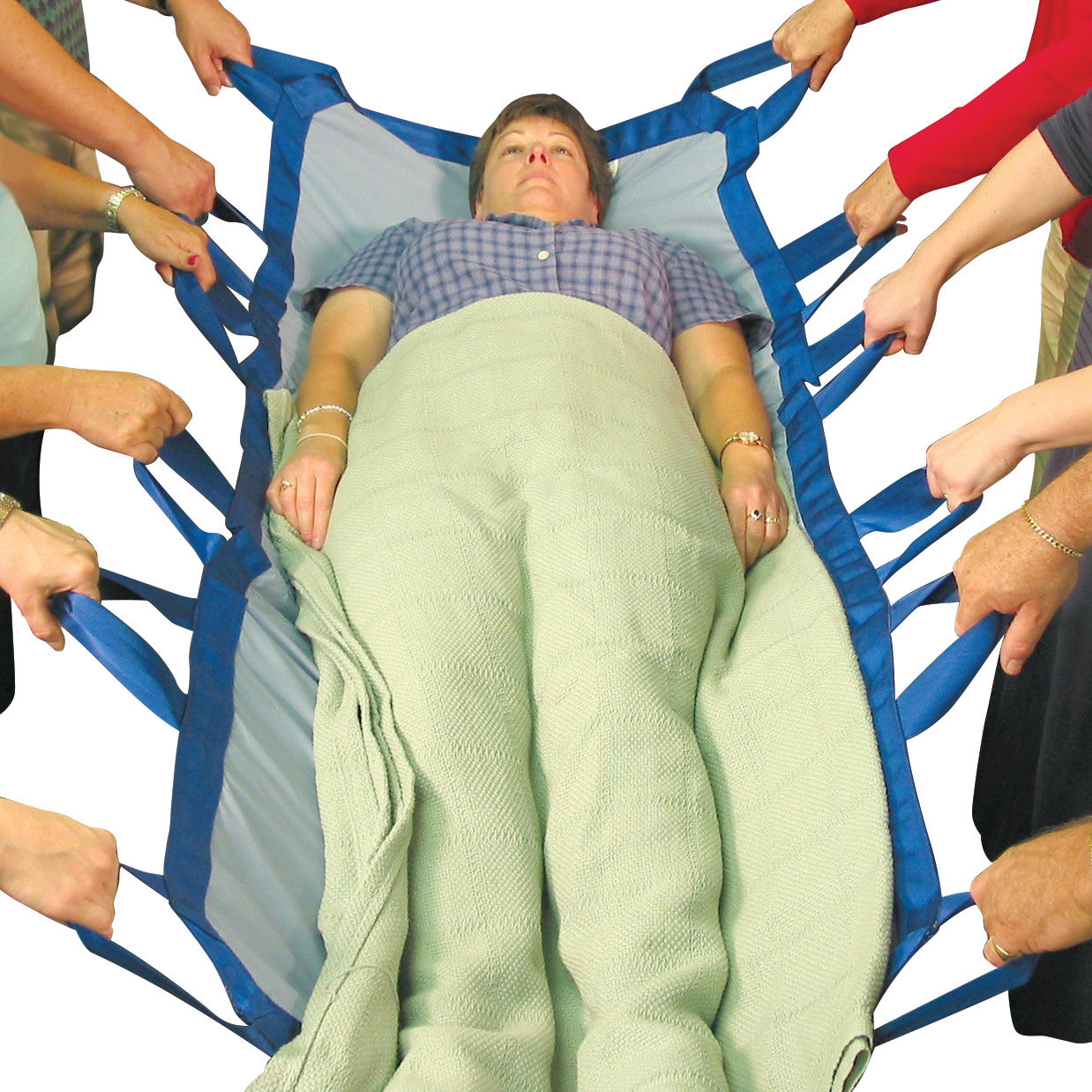 A woman lies on the SkiL-Care Bariatric Turner, held by multiple people using blue handles, with a light green blanket over her.