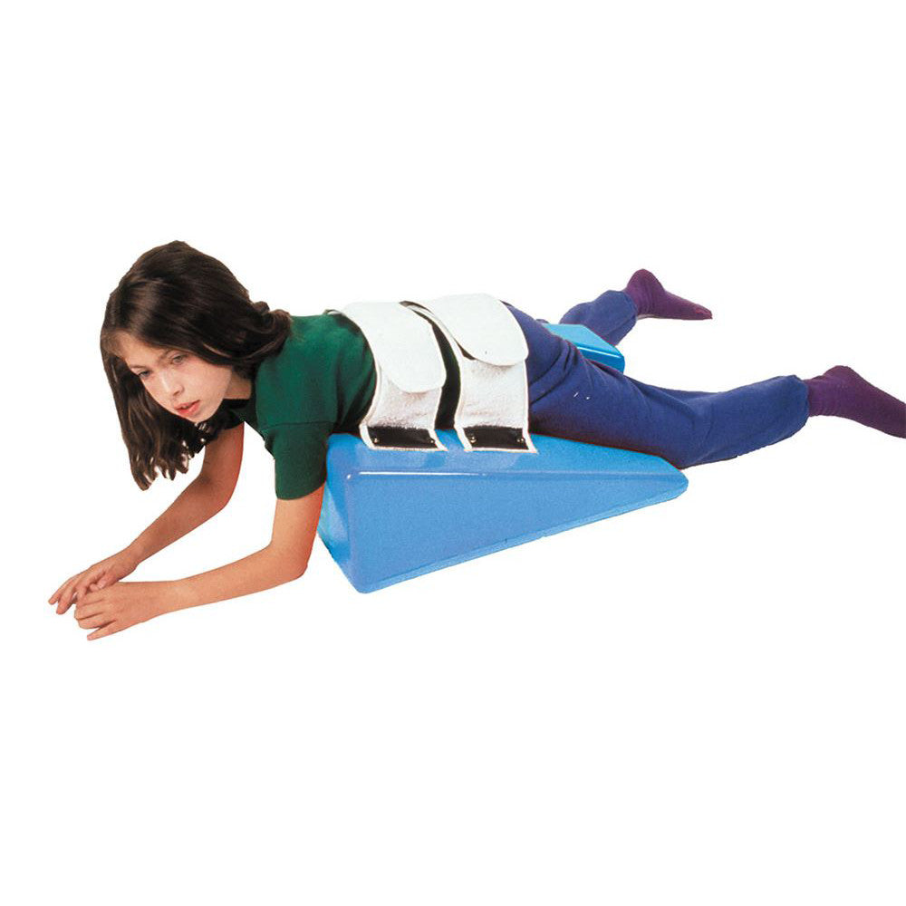 A child lies on a blue Skillbuilders Strap Wedge, secured with white straps, wearing a green shirt and blue pants.