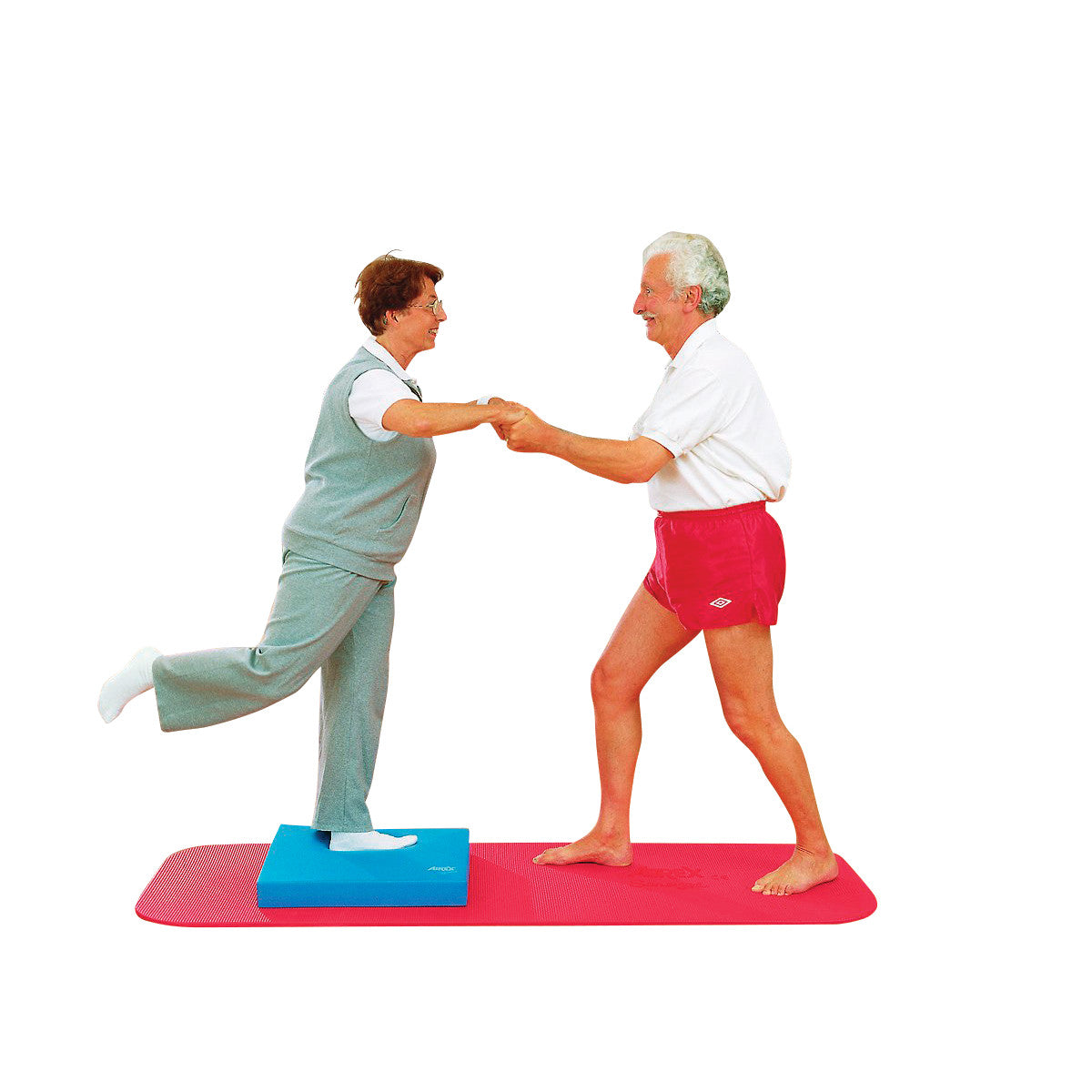 Two elderly people exercise with the AIREX Balance Pad. One stands on the pad, lifting a leg, while both hold hands for support.