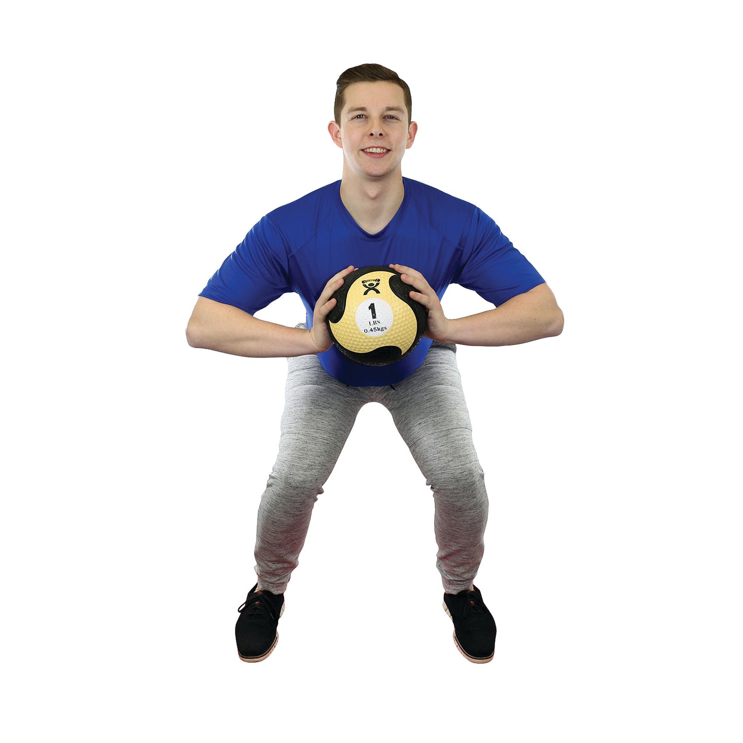 Man holds a CanDo Rubber Medicine Ball while squatting, wearing a blue shirt and gray pants on a white background.