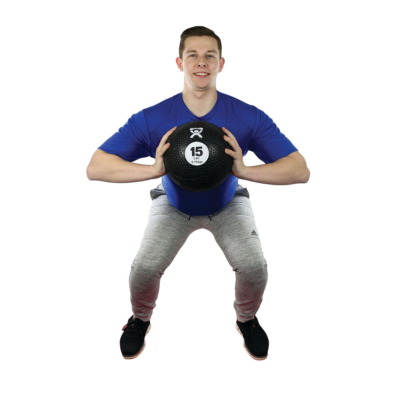 A person exercises with a 15-pound CanDo Rubber Medicine Ball, wearing a blue shirt and gray pants against a white background.