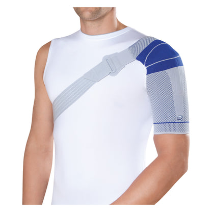 A person wearing a white shirt uses a Bauerfeind OmoTrain S shoulder support brace with a strap over the shoulder and chest.
