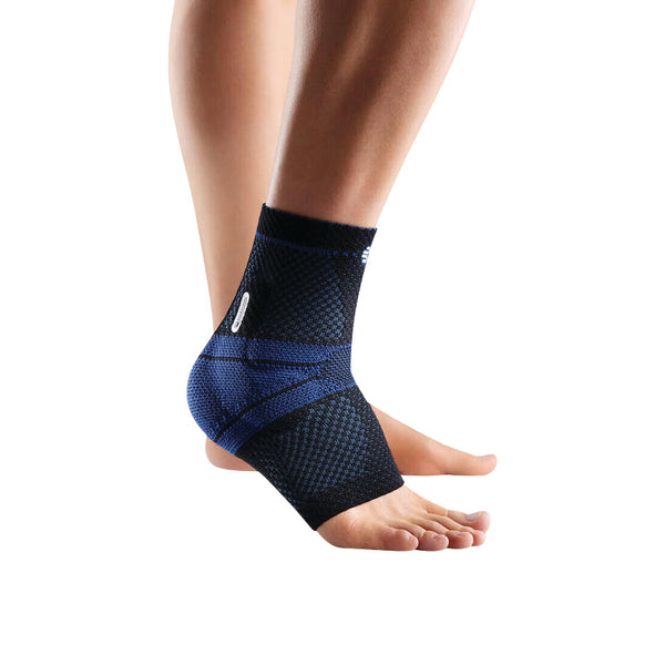 A person wears the Bauerfeind MalleoTrain Ankle Support, a blue and black compression brace, on their right foot against a white background.
