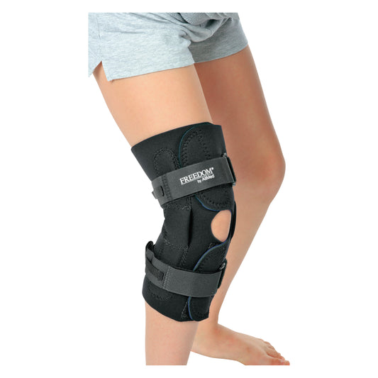 A person wearing an AliMed FREEDOM Pediatric Wraparound Knee Brace with adjustable straps and support panels over their knee.