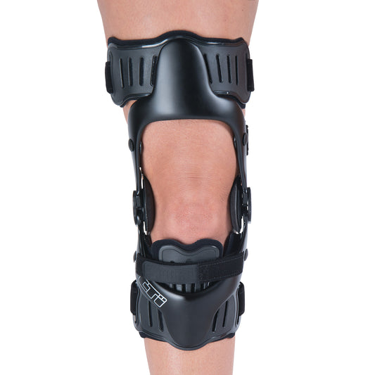 A person wears an ssur CTi OTS Knee Brace with PCL Support, featuring black straps and a rigid design for stabilization.