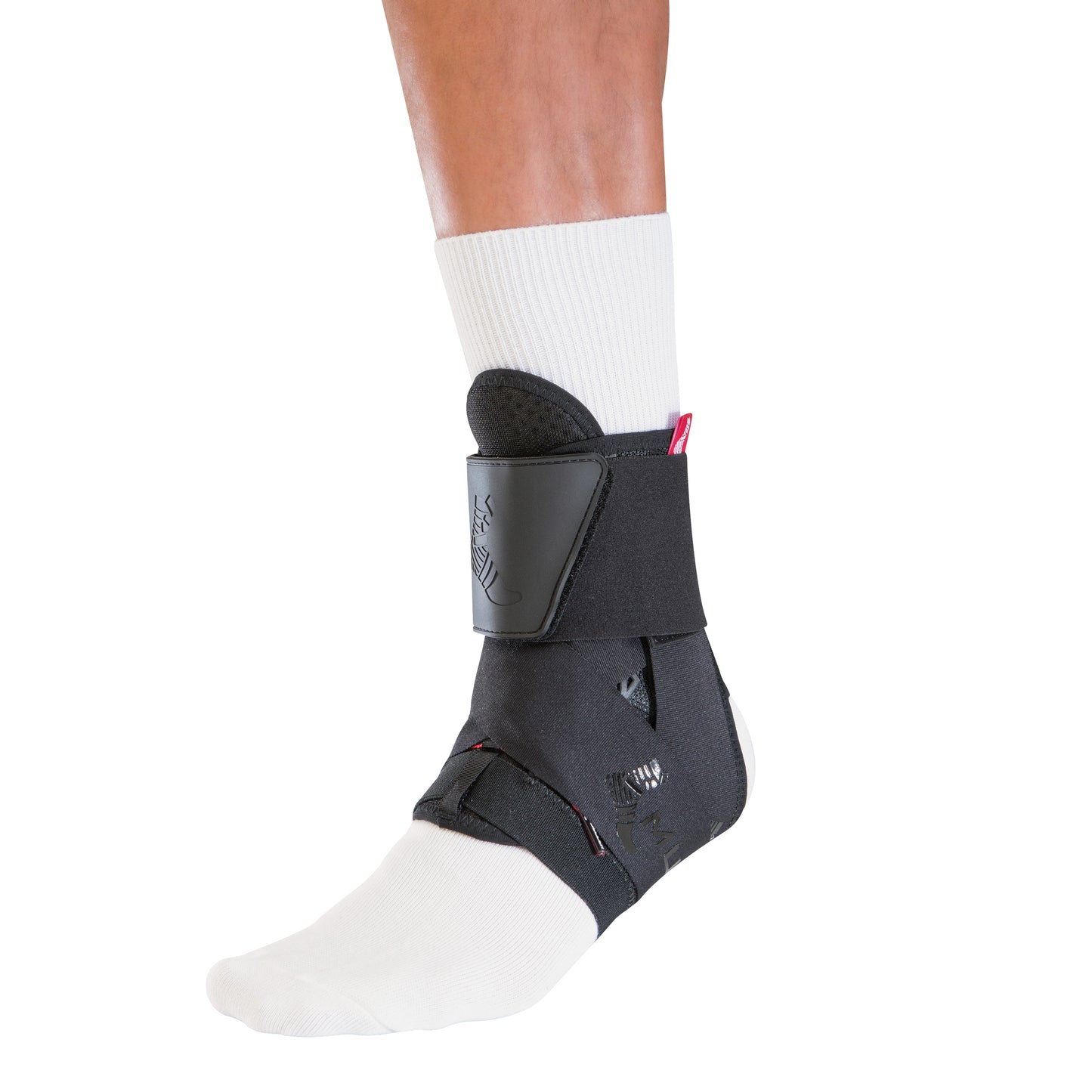 A person wears a Mueller The One Ankle Brace over a white sock. The black brace features straps and a supportive design.