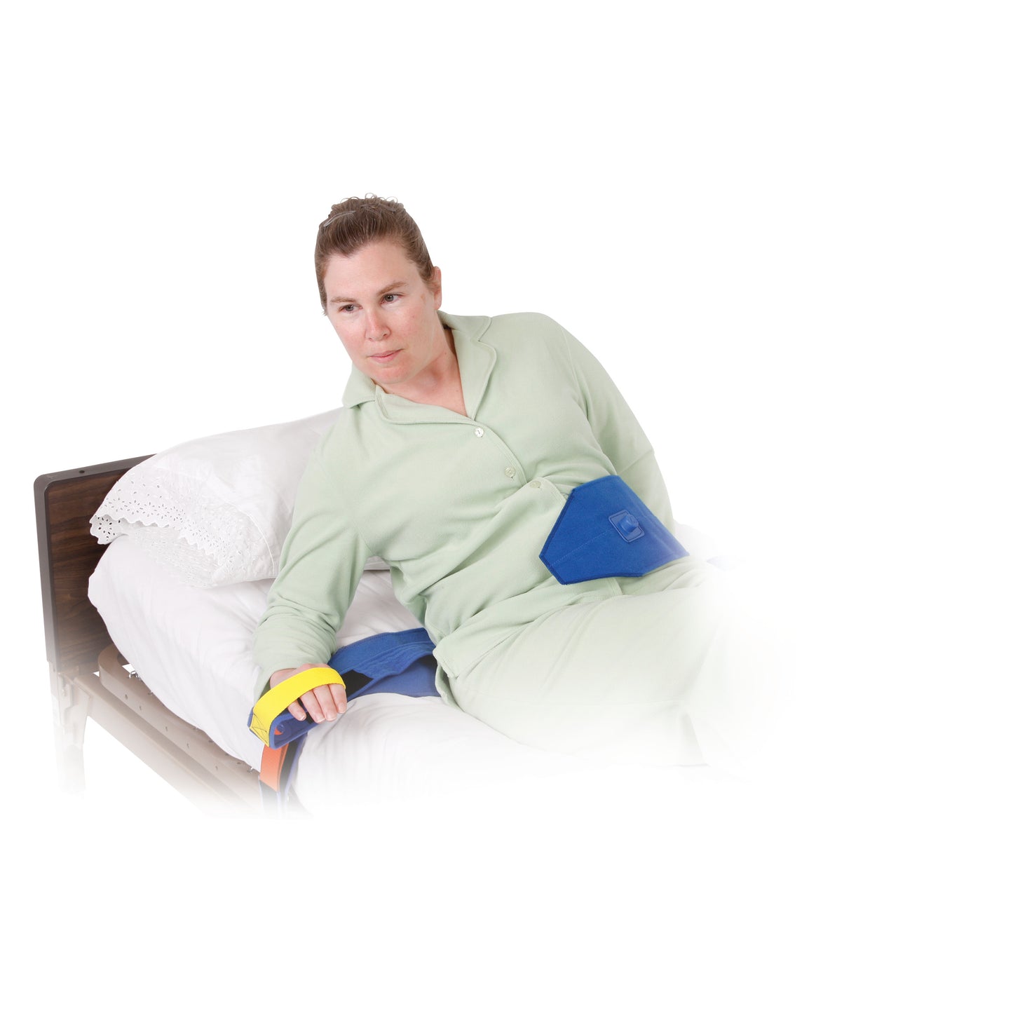 A woman in green pajamas is secured in bed with the AliMed Roll-Control Belt, featuring blue straps and colorful fasteners.