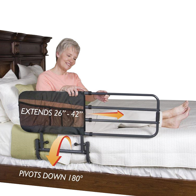 An older adult sits up in bed using the Stander EZ Adjust Bed Rail. The rail extends from 26" to 42" and pivots down 180 degrees.