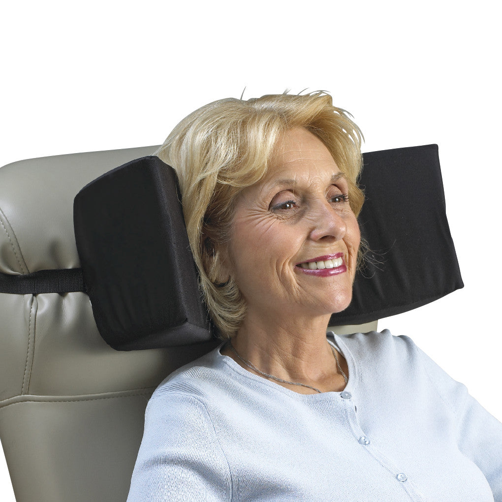 A woman uses the SkiL-Care Triangular Head Positioner, a black cushion secured to a chair, providing support for her head.