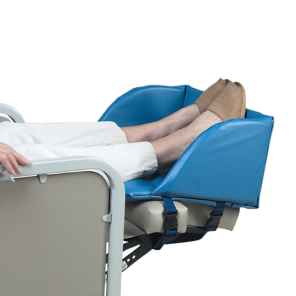 A person rests their legs on a SkiL-Care Geri-Chair Foot Cradle, featuring a blue padded support with buckled straps.