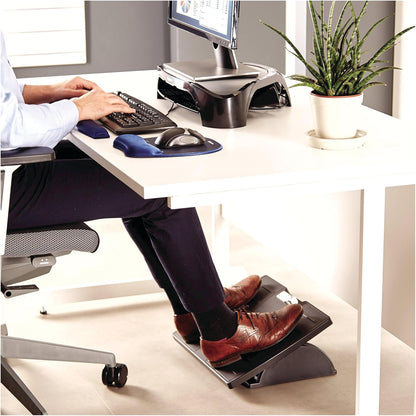 A person using a computer at a desk with an Adjustable Footrest with Microban while a plant sits nearby.