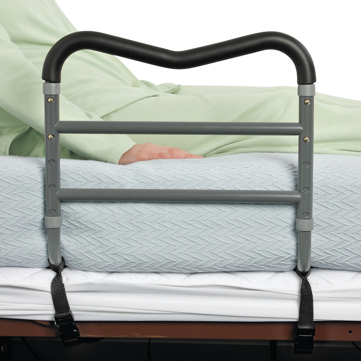 An AliMed AliRail Bed Rail is attached to a bed, providing support for a person in light green pajamas sitting on the mattress.