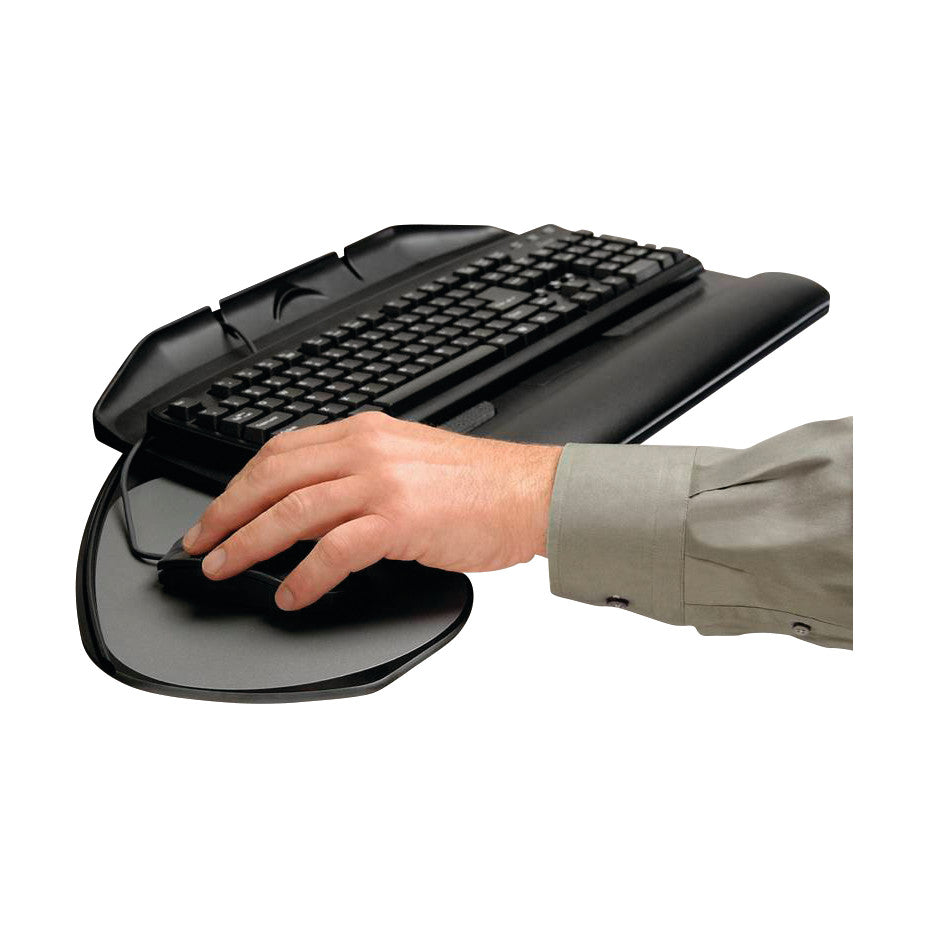 A hand uses a mouse on the Banana-Board Keyboard Tray, which holds a black keyboard on a curved platform.