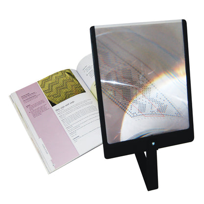 A Prop-It Portable Hands-Free Page Magnifier stands in front of an open book, enlarging text and images for easy reading.