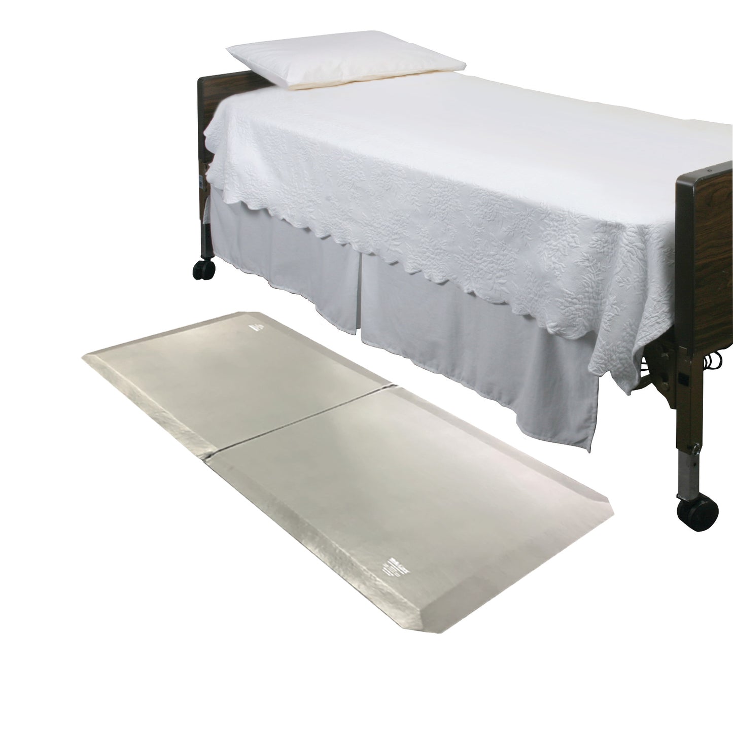 A bed with a white bedspread and pillow. The SkiL-Care SafeSide Bi-Fold Fall Mat is placed on the floor beside it.