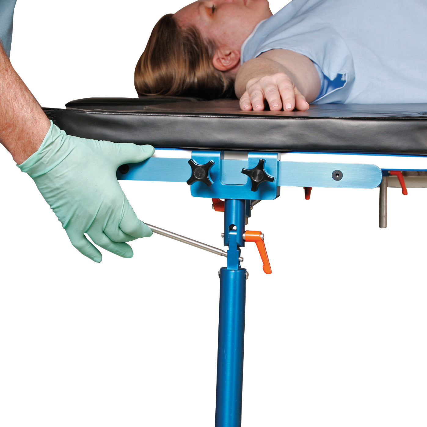 A person adjusts the height of an AliMed Pneumatic Hand Table Leg. A patient lies on a table with a cushioned surface.
