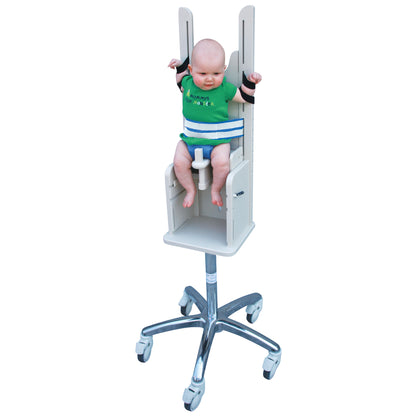 A baby is secured in a Pedia Poser, a medical imaging chair with straps and a metal base with wheels, designed for stability.