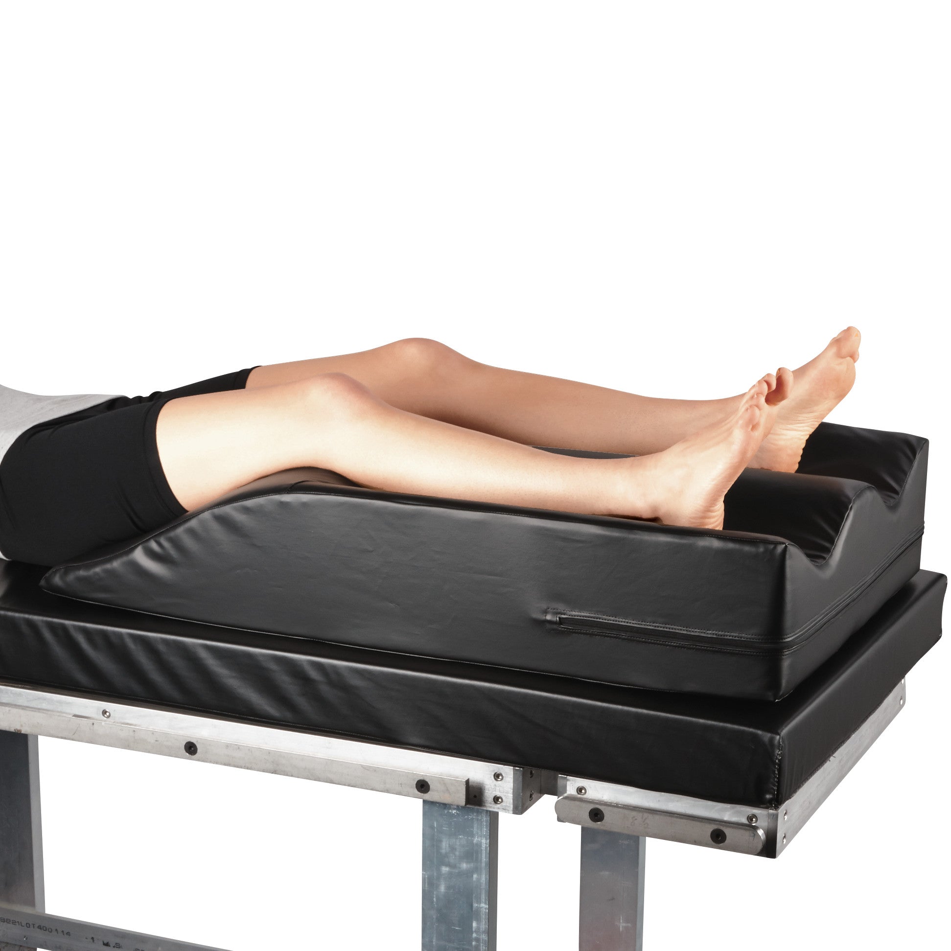Person's legs resting on an AliMed Frogger Vein Harvesting Positioner, a black wedge cushion designed for leg support.