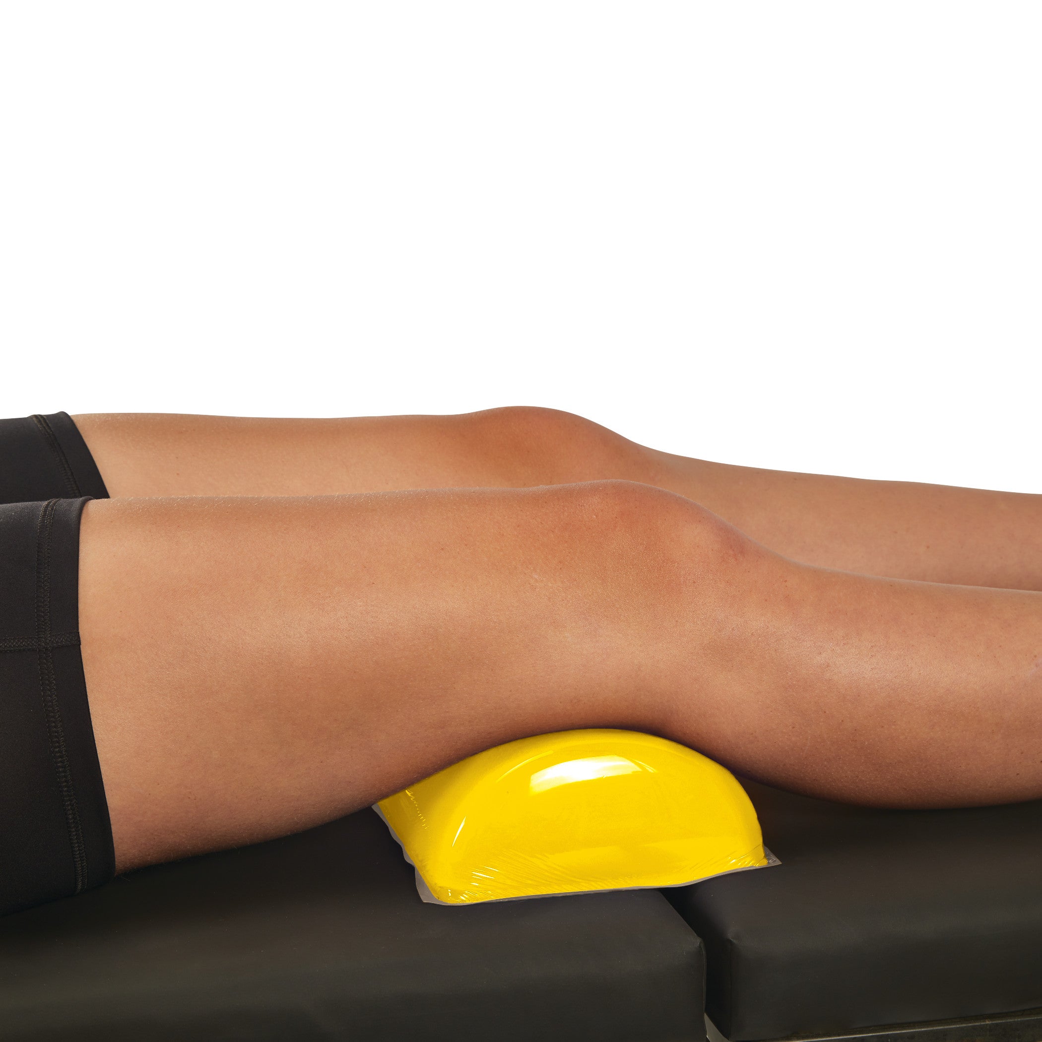 Two legs rest on a black surface with a yellow AliMed AliLite Dome Positioner placed under the knees for support.