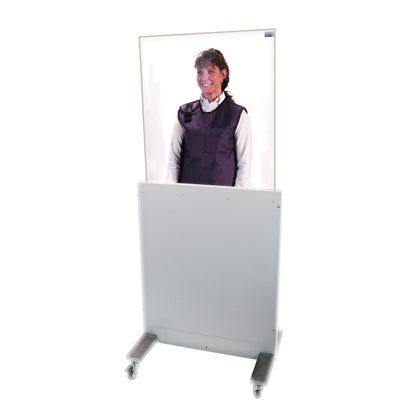 A person stands behind a movable, transparent RayShield Adjust-A-Height Barrier on wheels, wearing a protective vest.
