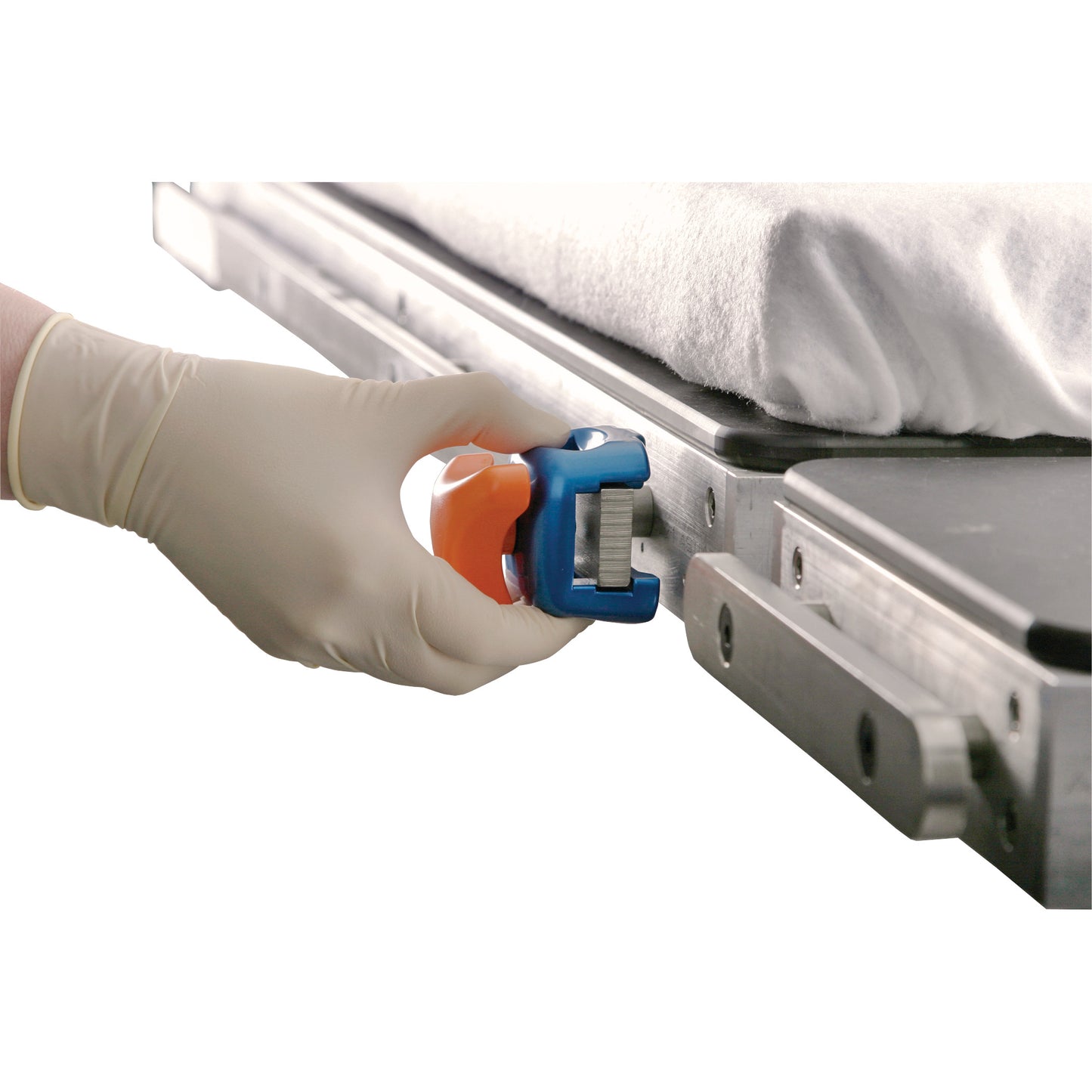 A hand in a glove holds the AliMed FREEDOM Flat Blade Socket near a metal rail on a medical table with a white sheet.