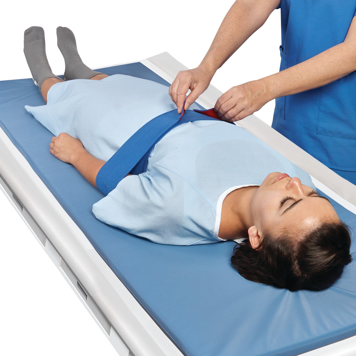 A person is on a table with an AliMed MRI/CT Arm Holder, featuring a blue strap securing their arms, guided by a caregiver.