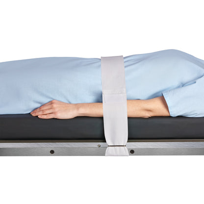 A person lies on a table secured with a Halyard Operating Room Table/Stretcher Strap over their body, wearing a light blue garment.