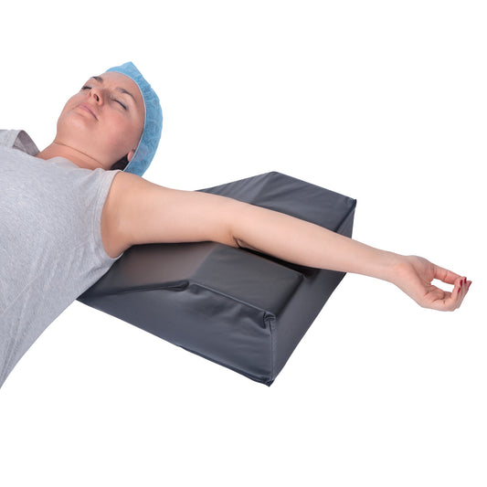 A person rests their arm on an AliMed Foot/Hand Prepper, a wedge-shaped, black cushion for positioning during procedures.