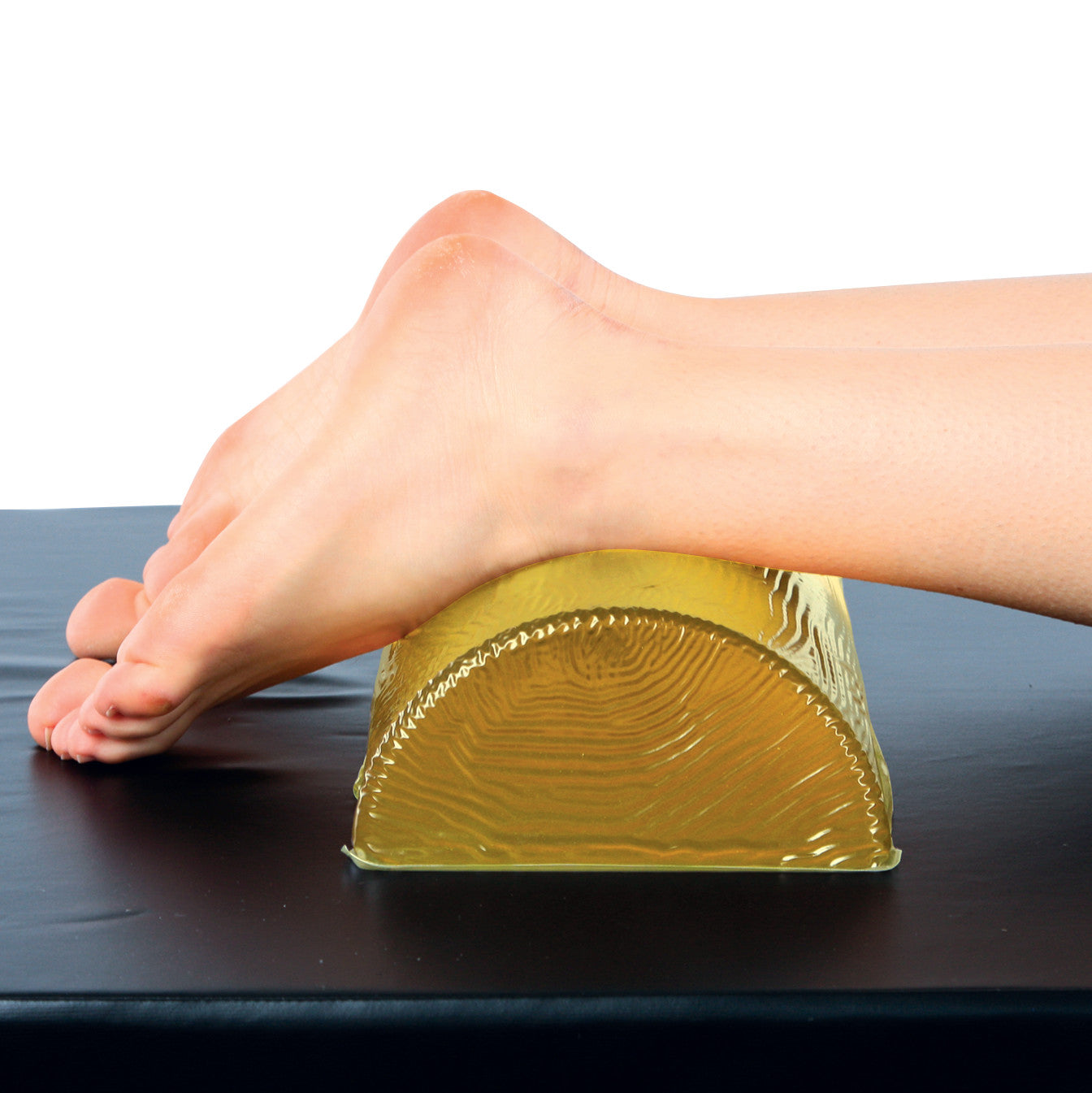 A foot rests on the AliMed AliGel Dome Positioner, a semi-circular yellow gel cushion, on a black surface.