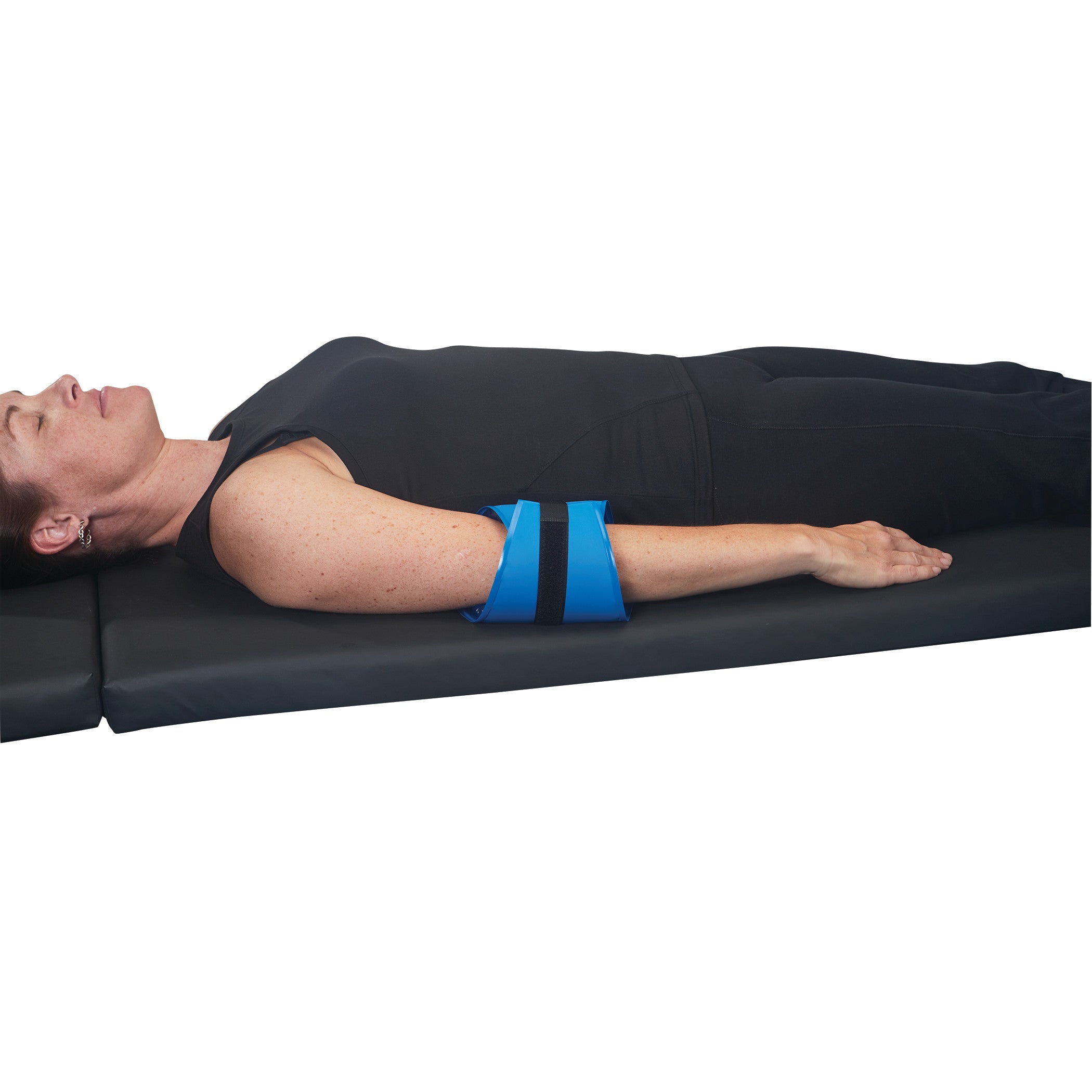A person lies on their back, using the AliMed AliBlue Gel Ulnar Nerve Protector on their arm, resting on a black mat.