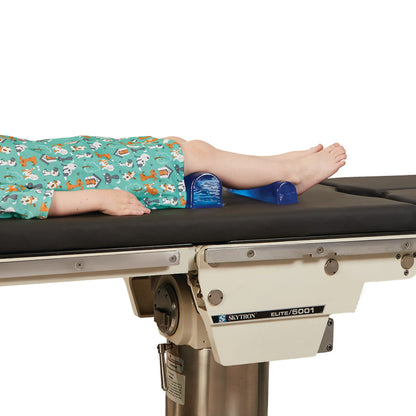 A child lies on a medical table with an AliMed AliBlue Gel Chest Roll under their knees, wearing animal print clothing.
