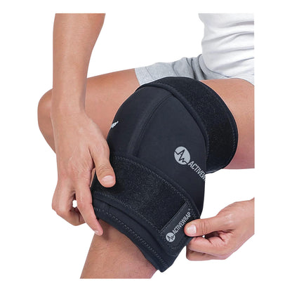 A person applies an ActiveWrap knee brace, featuring adjustable straps and black neoprene material, to their knee for support.