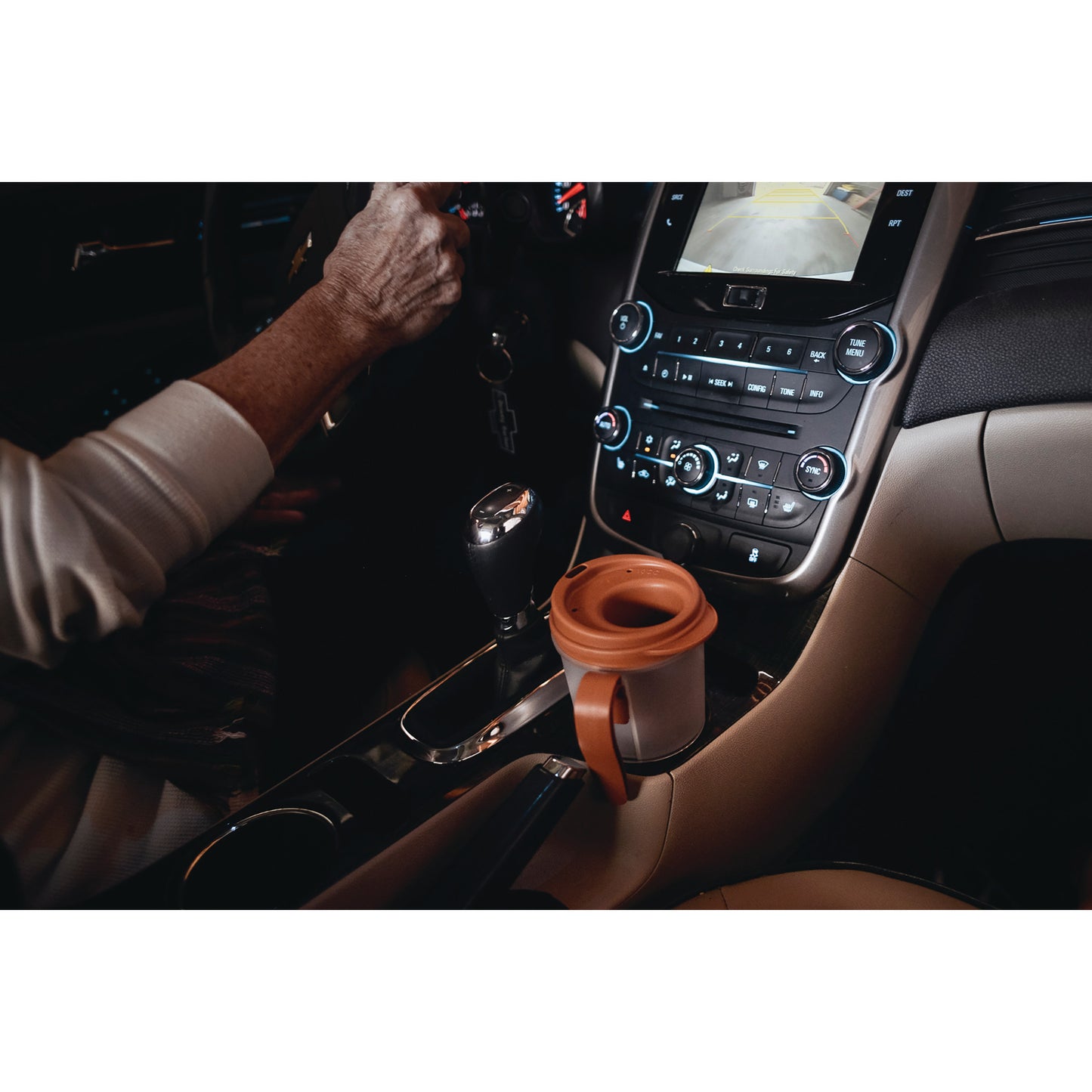 A person holds a steering wheel near a Provale Cup placed in a car's cup holder. The dashboard and gear shift are visible.