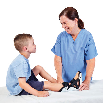 A nurse smiles at a child wearing an AliMed Classic Pediatric Night Splint on their left foot while seated on a medical table.