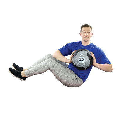 A person exercises with a CanDo Rubber Medicine Ball, marked with "20 lbs," wearing a blue shirt and gray pants.